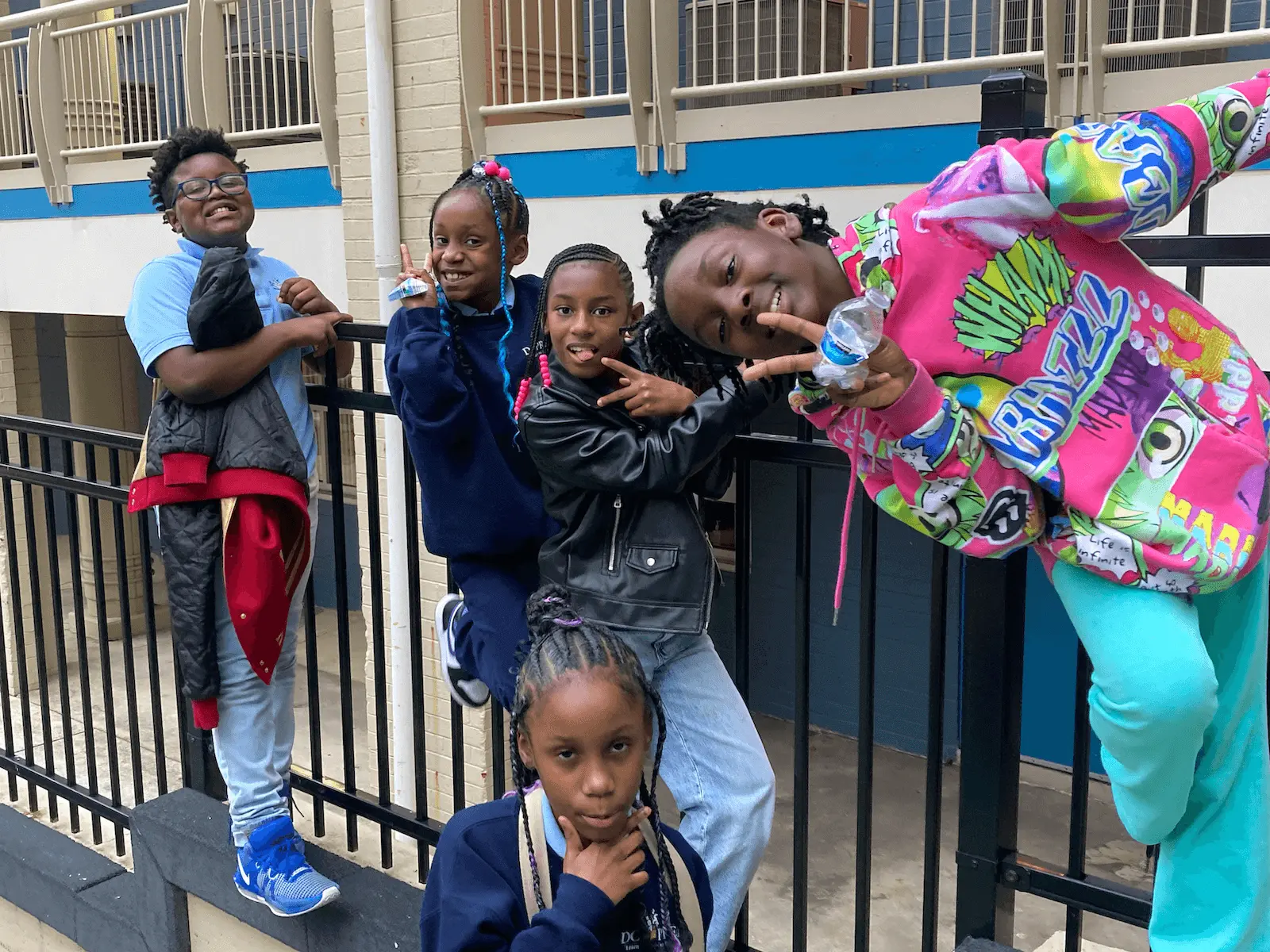 A group of young black school girls, smiling and posing for a picture together along a railing in a school environment